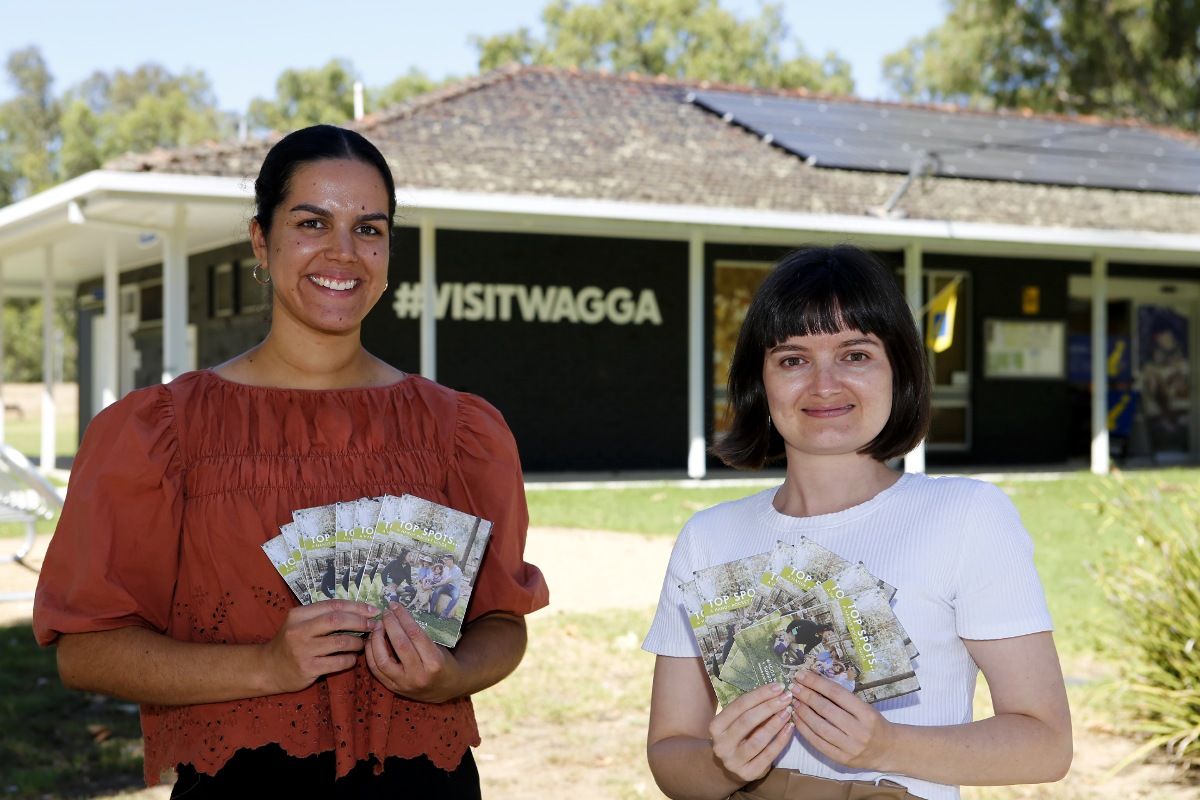 Two women standing near Visitor Information Centre in Wagga, holding copies of the 2024 Top Spots guide