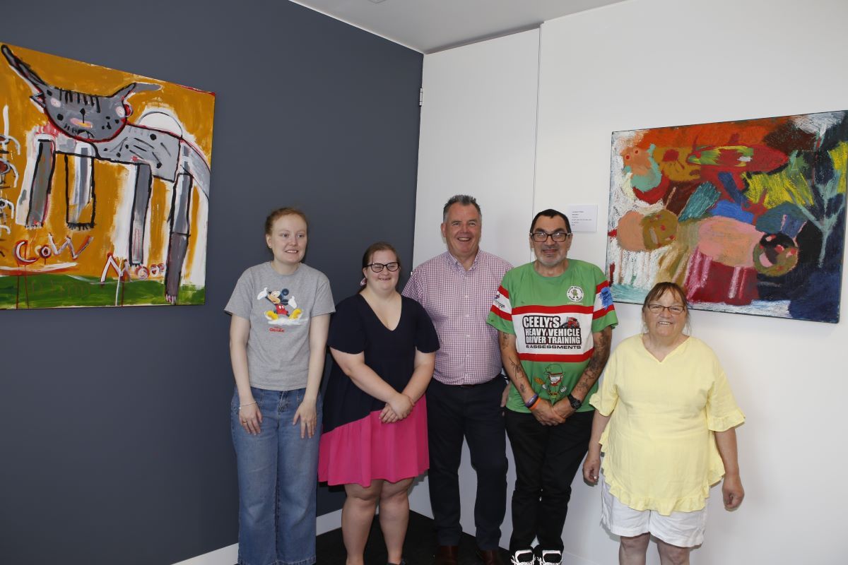 A group of people standing in an office between two bright, colourful artworks. 