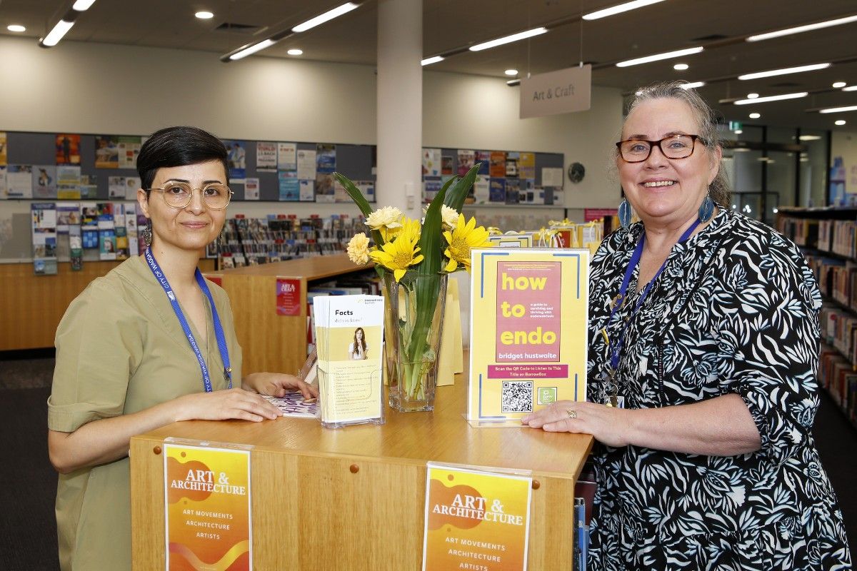 Two woman next to a display of endometriosis theme books, pamphlets and signs