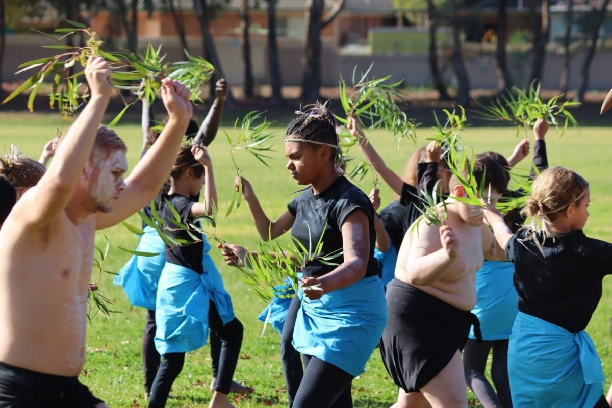 First Nations youth wearing traditional dress and carrying sprigs of gum trees, dancing