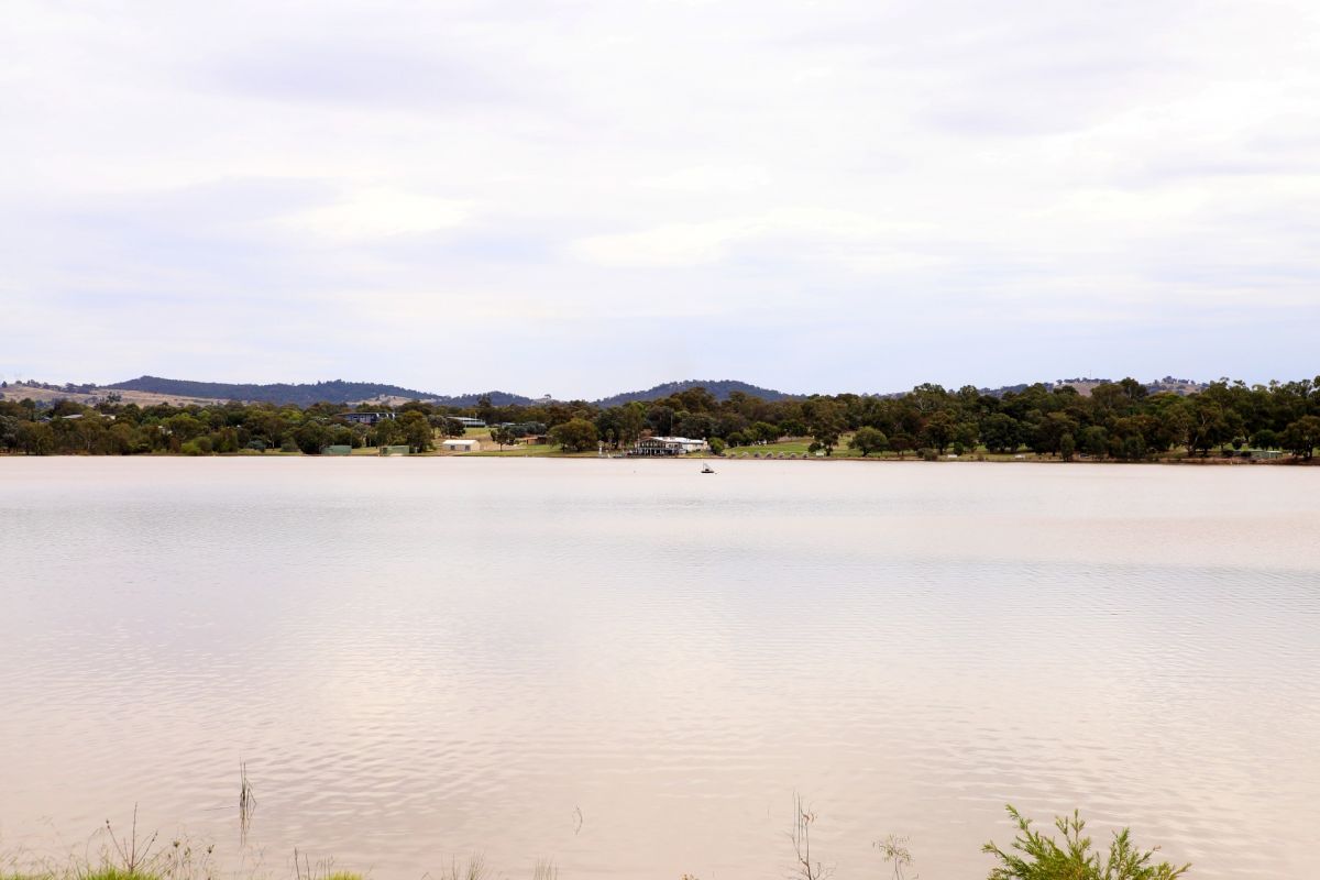 Lake in sunshine in the foreground, with a white building on the opposite shore in the background.