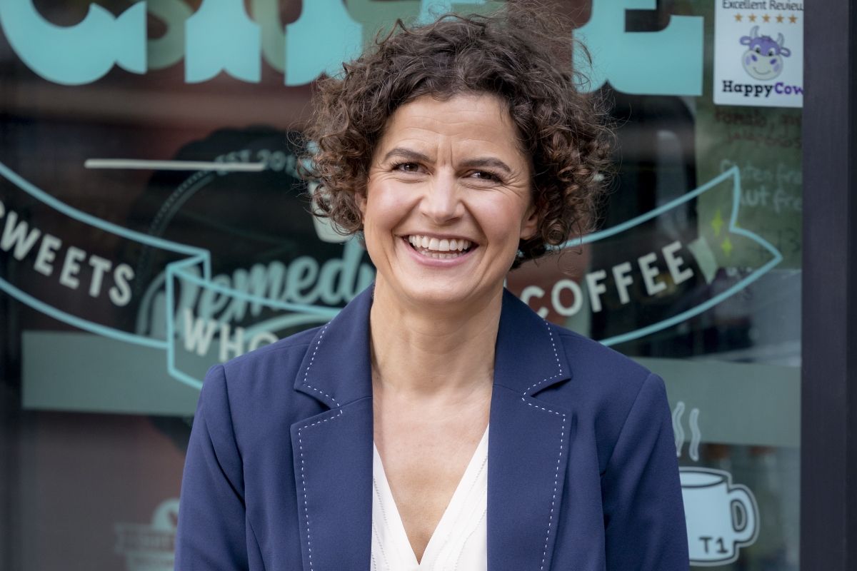 Woman smiling to camera, with the front window of a cafe visible in the background.