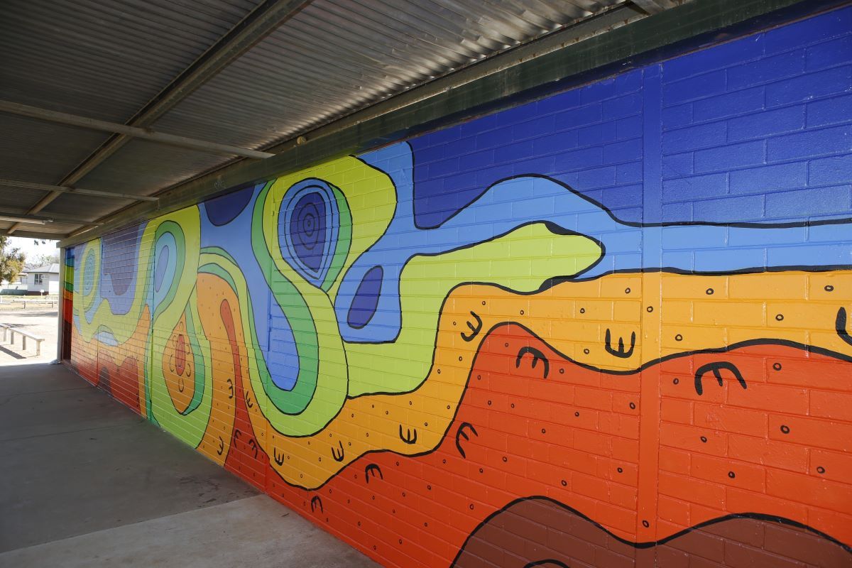 Colourful design of a serpent shedding its skin to symbolise rebirth into a safe place, in a mural on the side of an amenities block at a football oval.