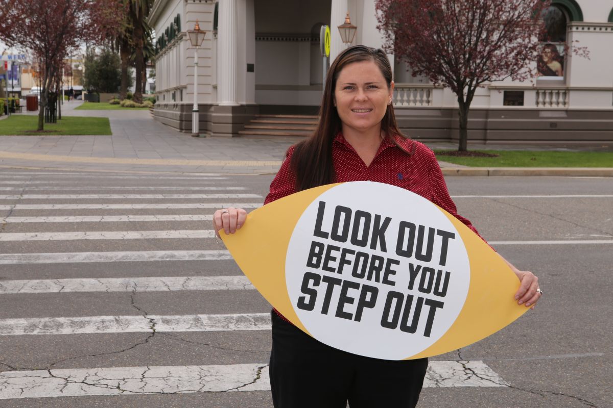 Woman holding sign, zebra crossing in background, old Wagga Council Chambers in background