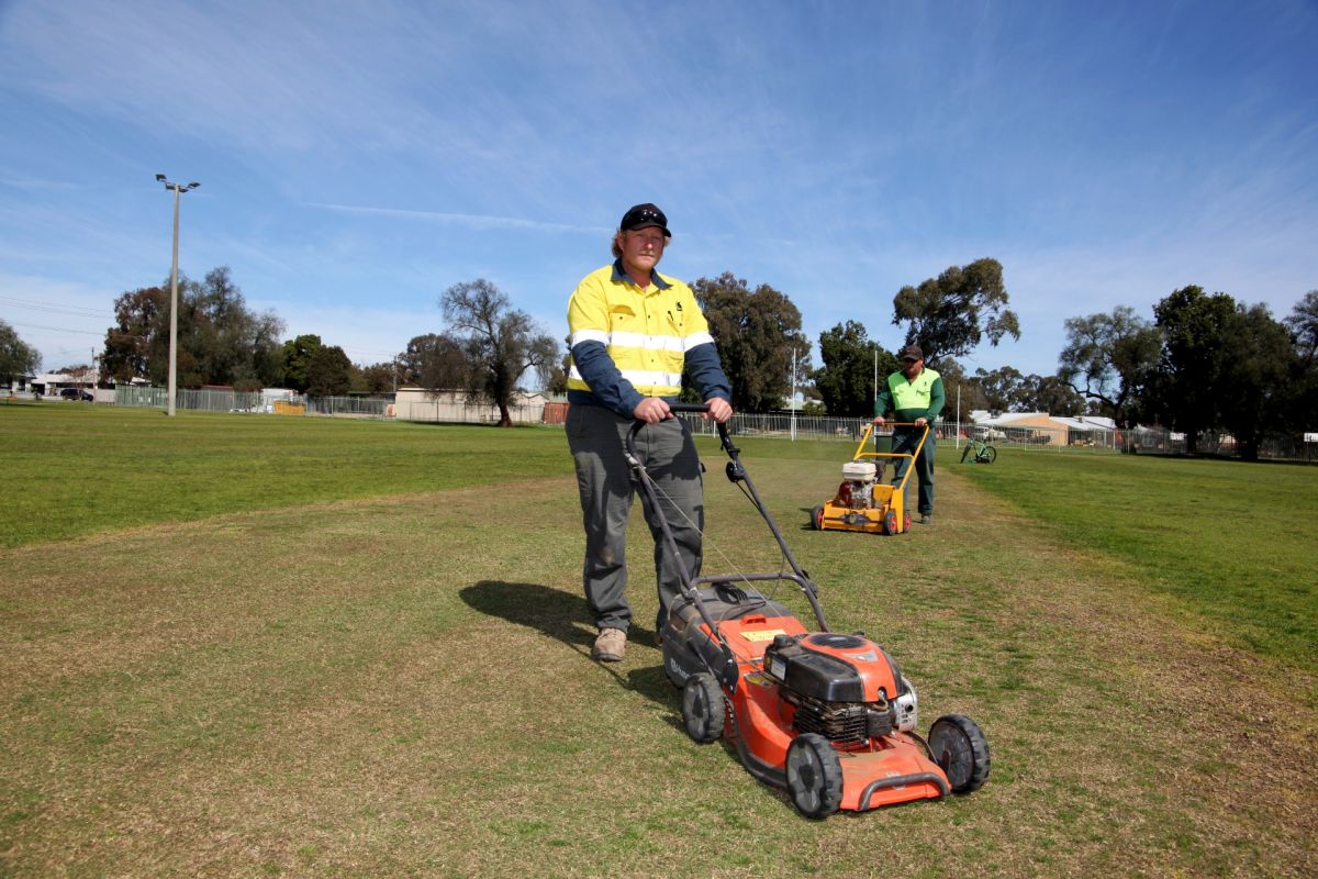 two men pushing mowers on turf cricket pitch