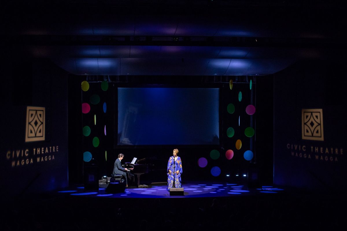 female performer on stage with pianist in background