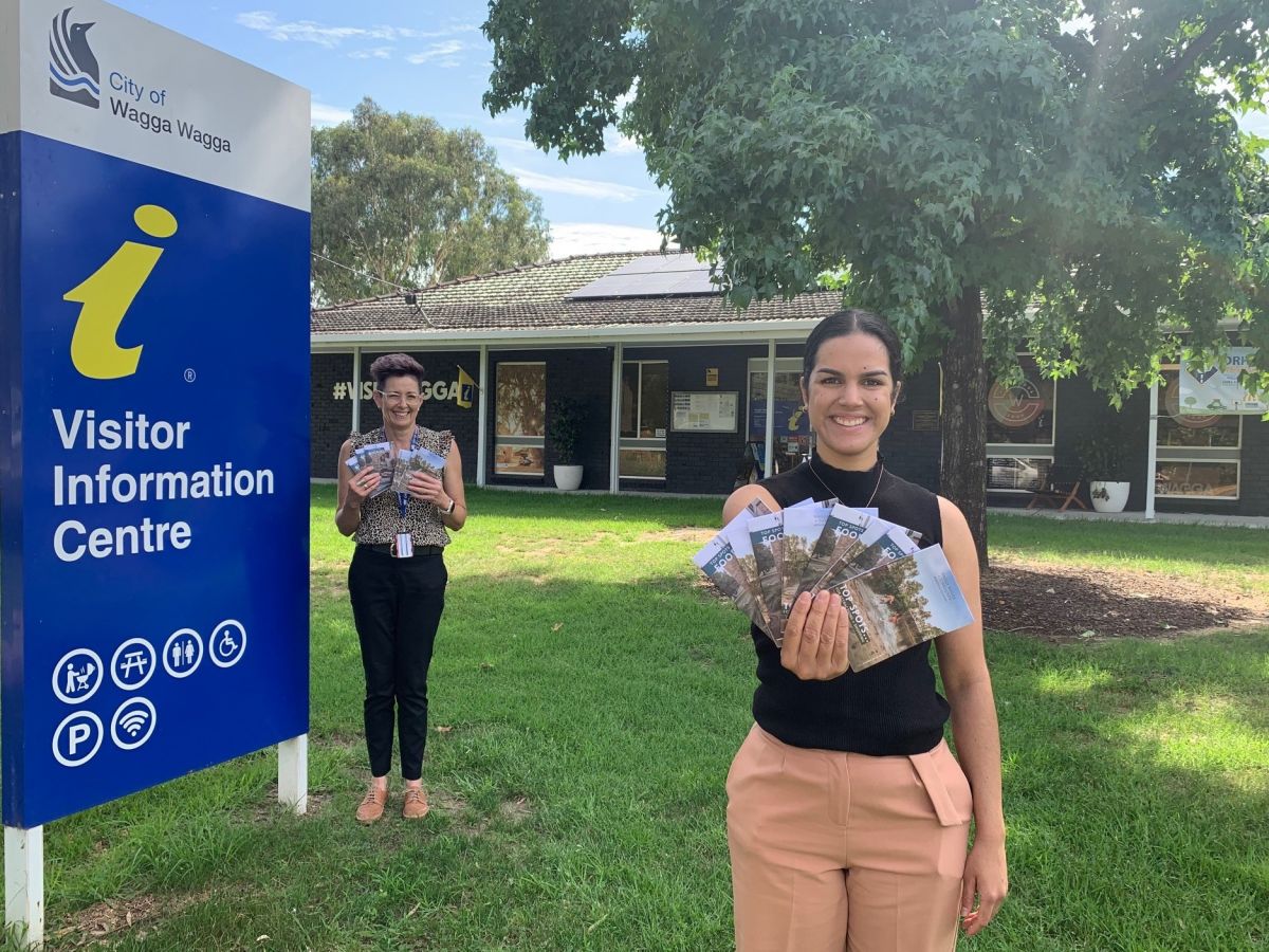 Two women holding booklets in front of a building