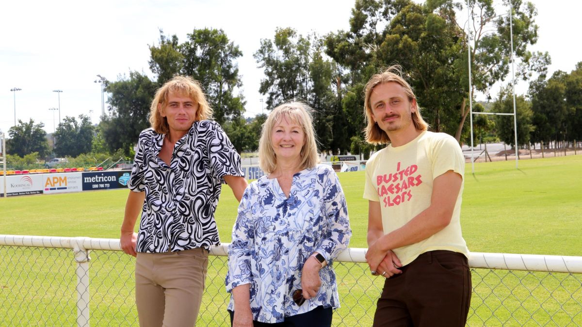 Oli and Louis Leimbach with Jenny McKinnon, leaning on fence of football grounds