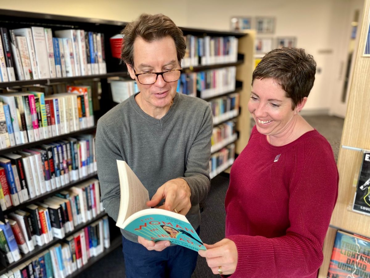 A man and a woman look at a book amongst bookshelves