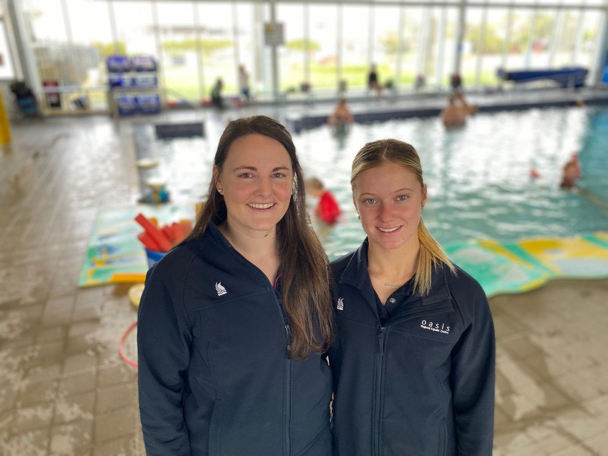 Two young women stand together in an indoor pool