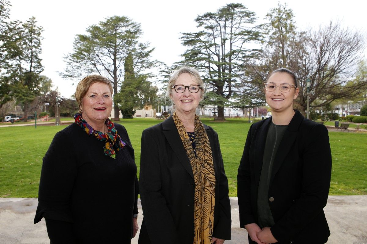 Three women standing on stage with park in background