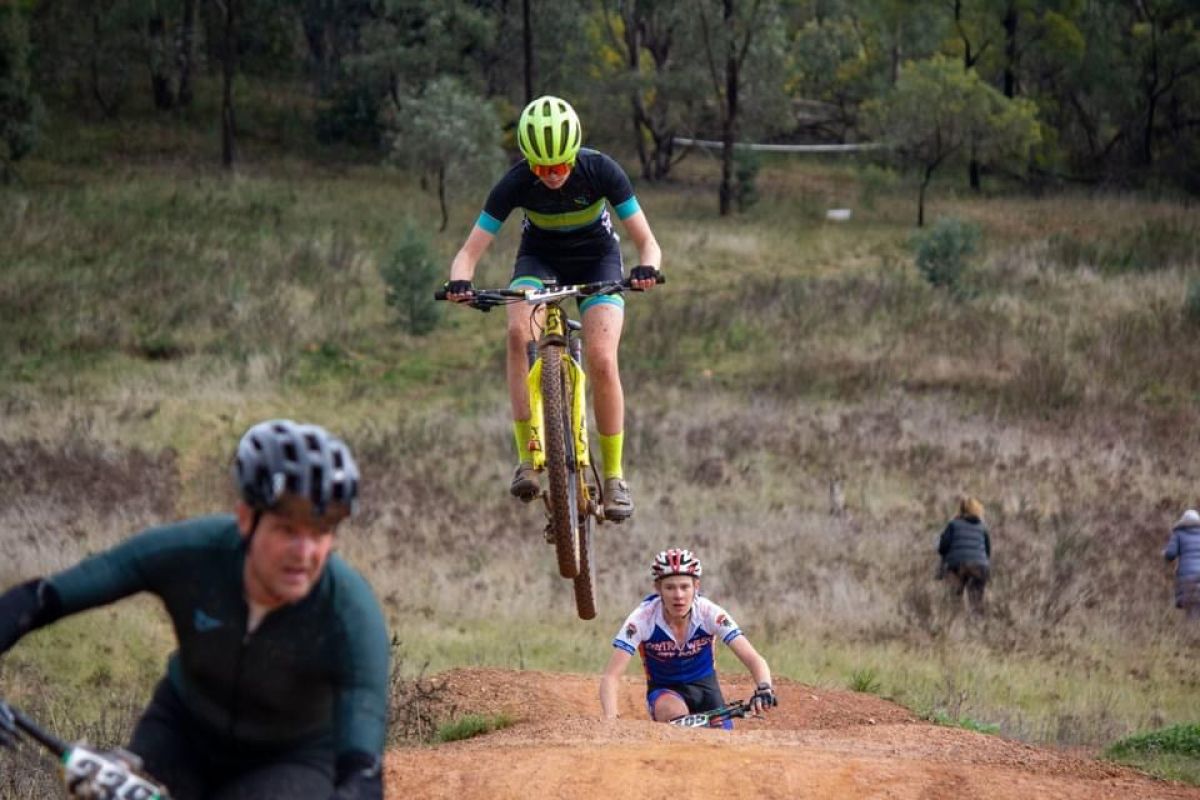 Mountain bike rider on jump on course at Pomingalarna Reserve with other riders in foreground and background