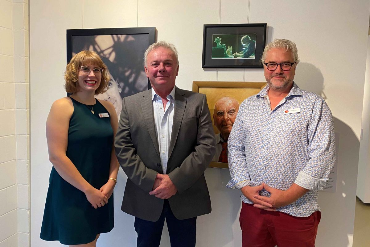 Woman and two men standing in front of portraits on wall