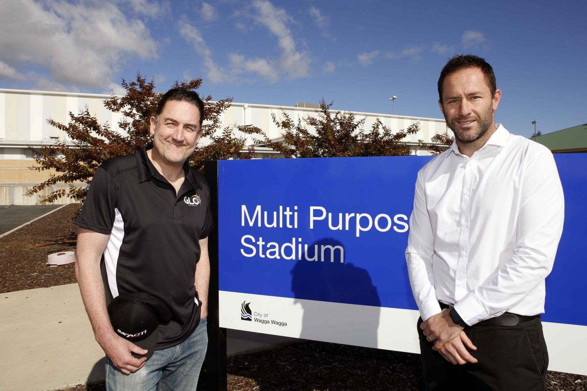 Two man standing beside blue sign with Multi Purpose Stadium written on it