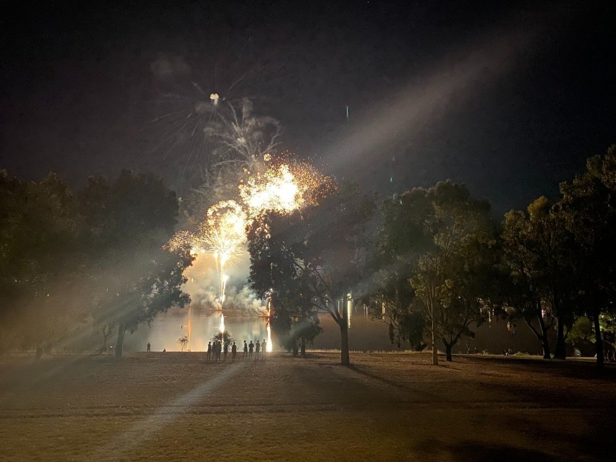 Night time, people standing on foreshores of Lake watching fireworks show over the lake