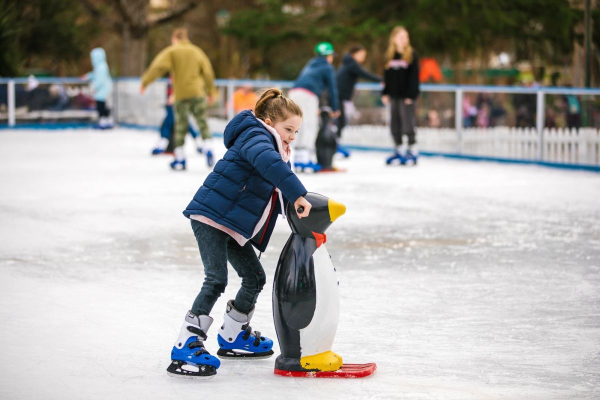 A young girl skating on a pop-up outdoor ice rink, with other people skating in the background 