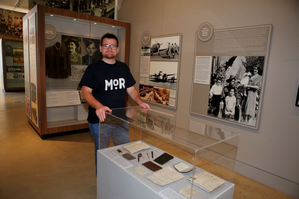 A man stands near a case with historical items in a museum.