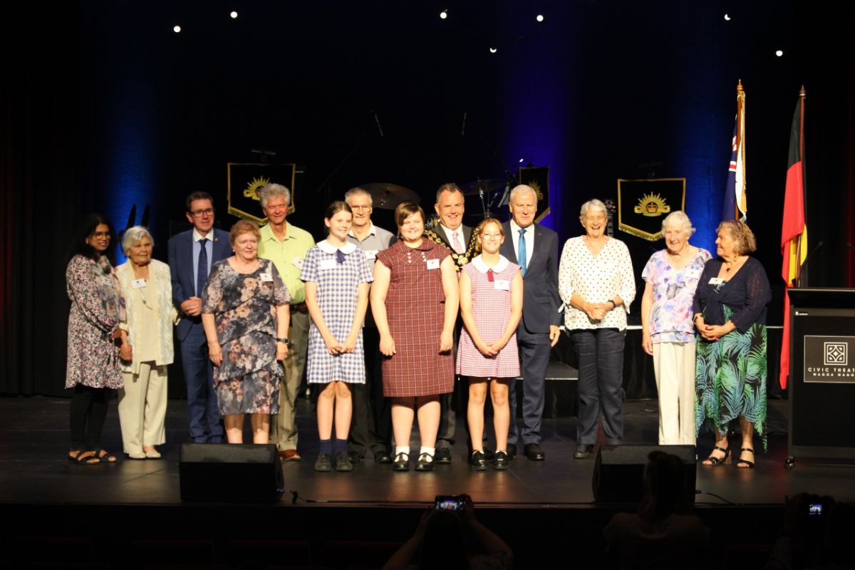 Group of people, including school students in uniform, and adults in suits standing on stage at Civic Theatre