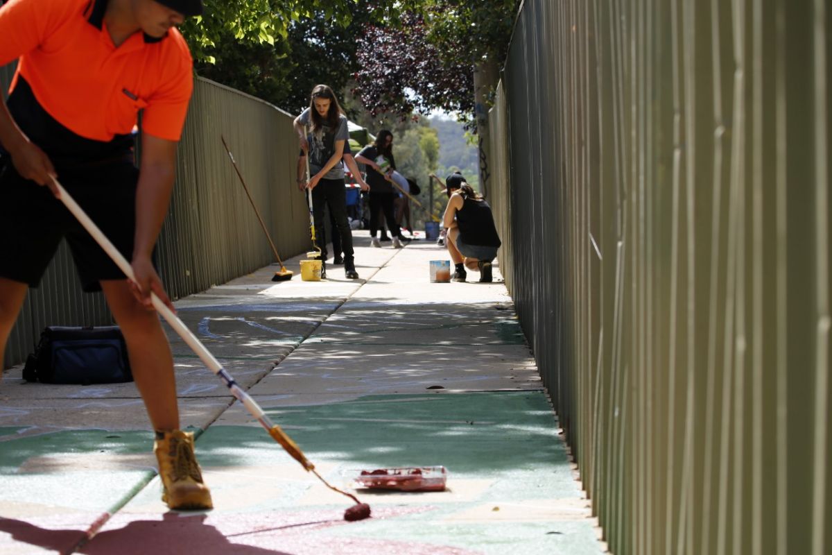 Field of depth shot along the laneway between Dove Street and Hunter Street in Mount Austin, Wagga Wagga. Students from Mount Austin High School are spread along the laneway at different spots and each use a paint roller to paint the pathway.