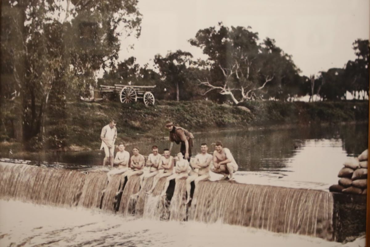 A photograph of a group of young people sitting on weir in a river. 