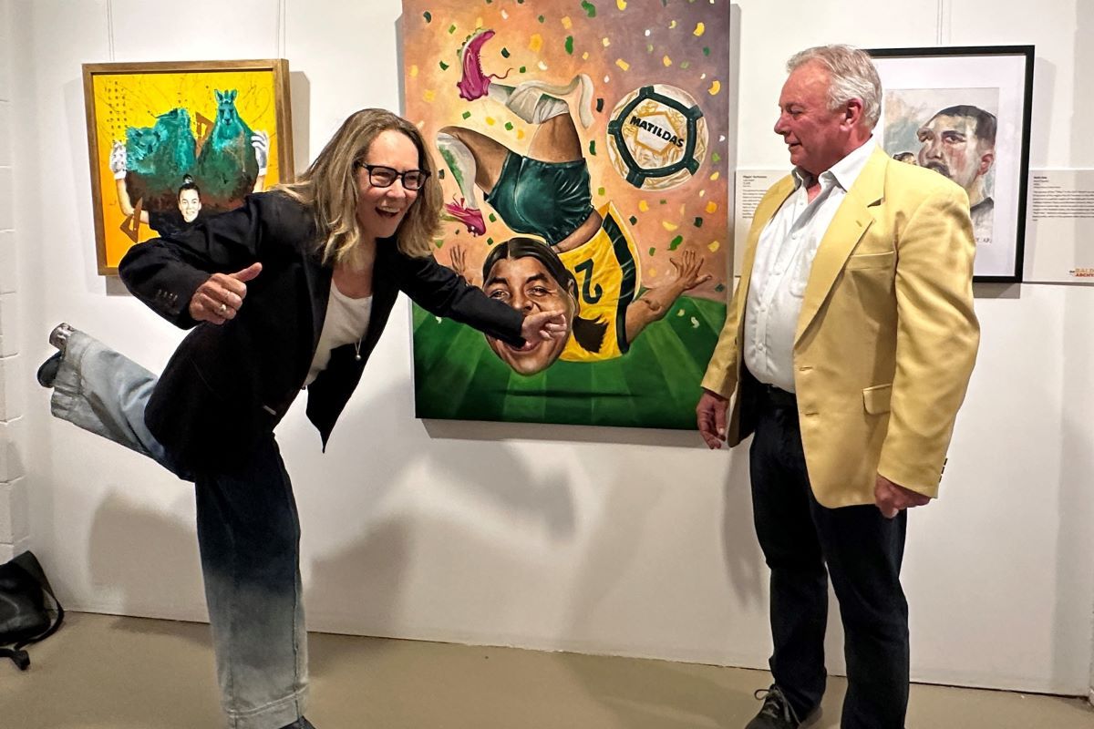 A man and a woman in an art gallery, the woman is in a flighty pose as the man looks on. 