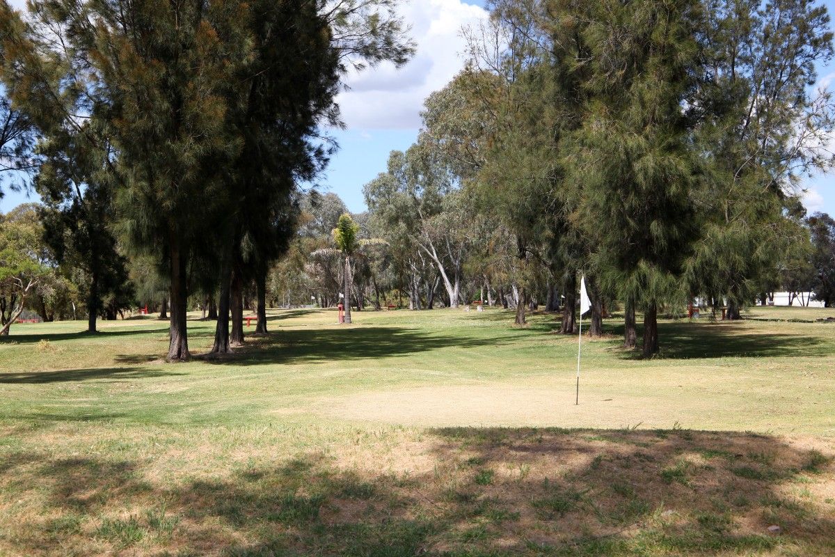 View down the fairway of a golf driving range, with trees on either side