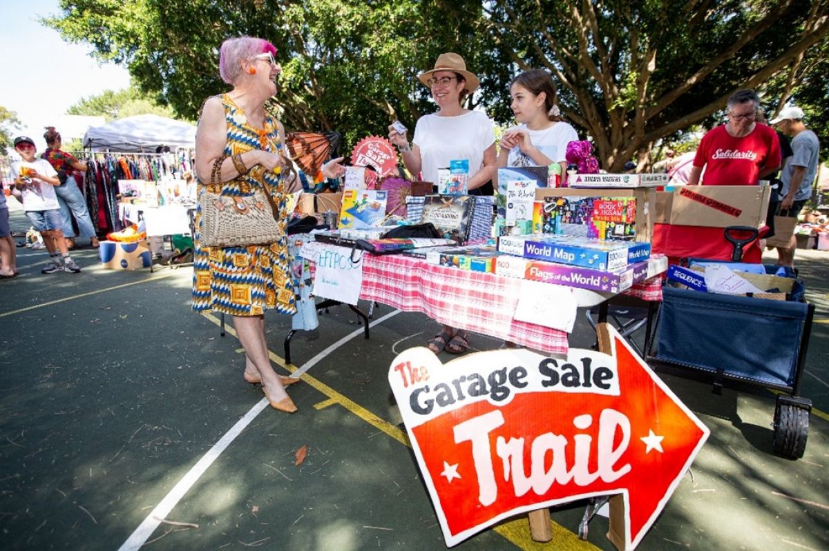 Woman looking at garage sale trail stall staffed by two