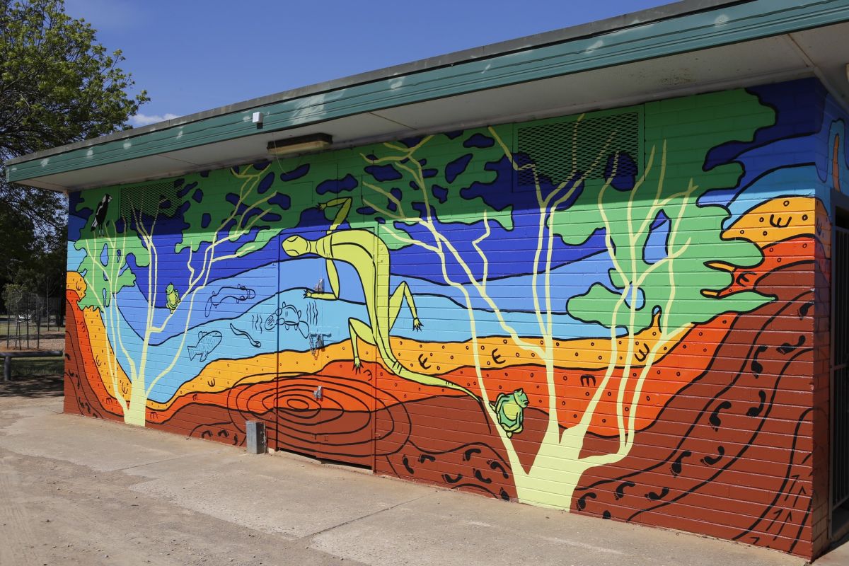 A colourful mural featuring First Nations themes and Wiradyuri storytelling on the side of an amenities block at a football oval.