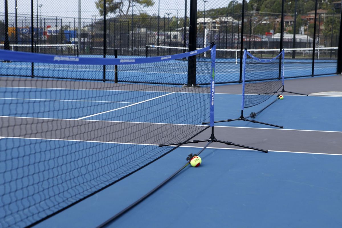 Two tennis balls sitting against temporary nets on two cushioned acrylic hard courts.
