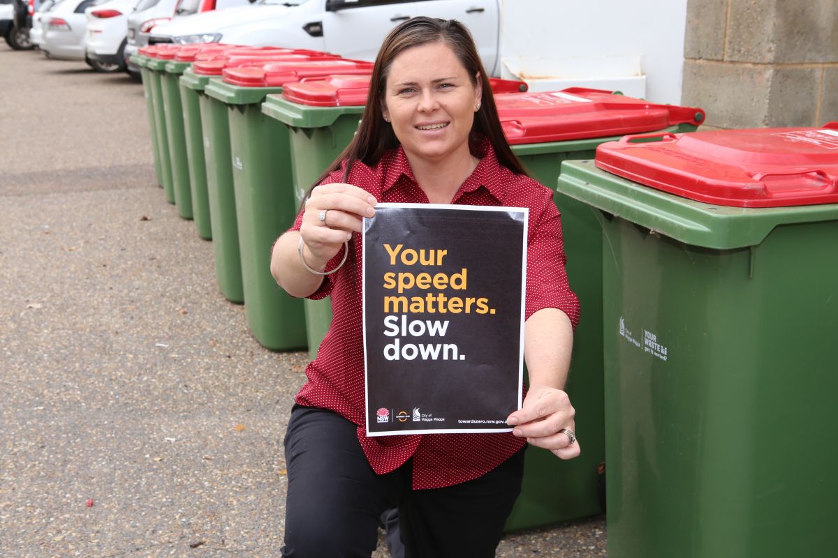 woman holding Slow Down poster next to red lid garbage bins