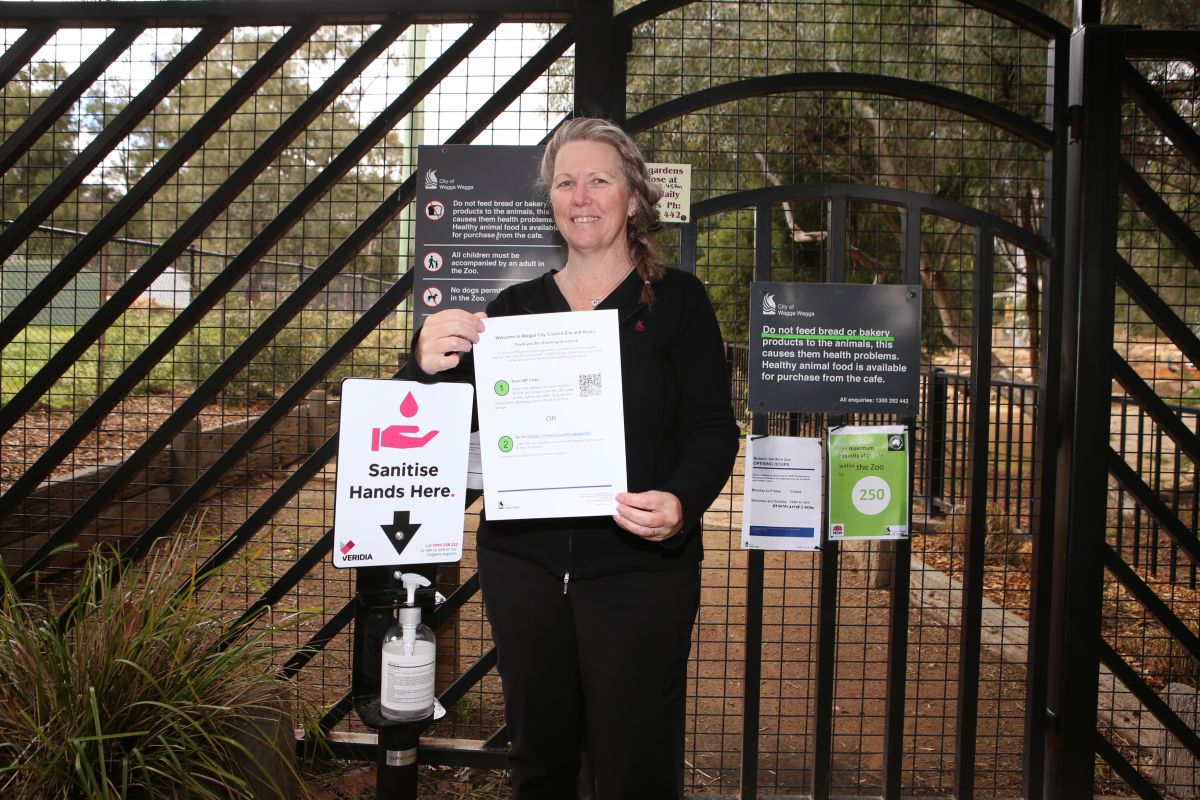 woman standing at gate of Zoo, holding sign with QR code symbol