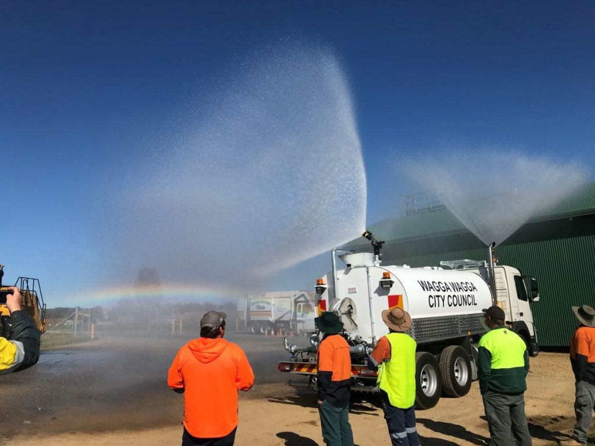 Group of people stand in front of water truck