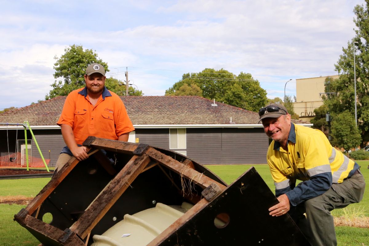 Two men in park about to lift section of modular pump track