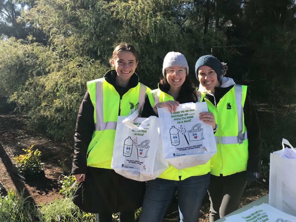 Three women outdoors holding white bags