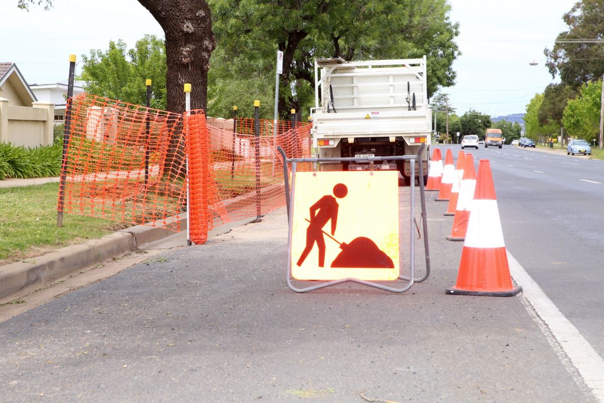 Newly cemented kerb behind orange plastic fencing with at work sign