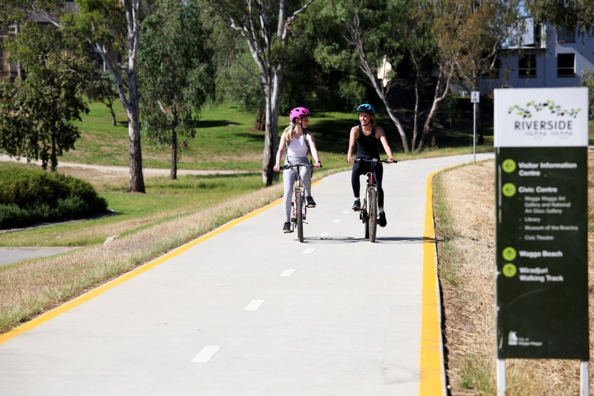 Two young women on bikes riding on cement cycle path
