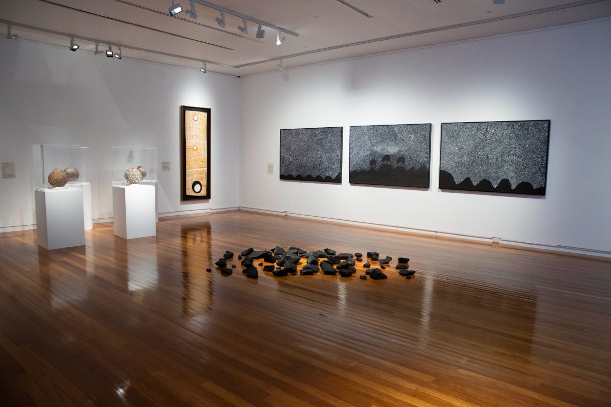 art installation featuring rock on timber floor and paintings on walls in background