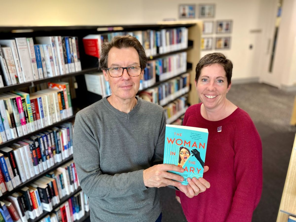 A man and a woman holding a book beside a bookshelf