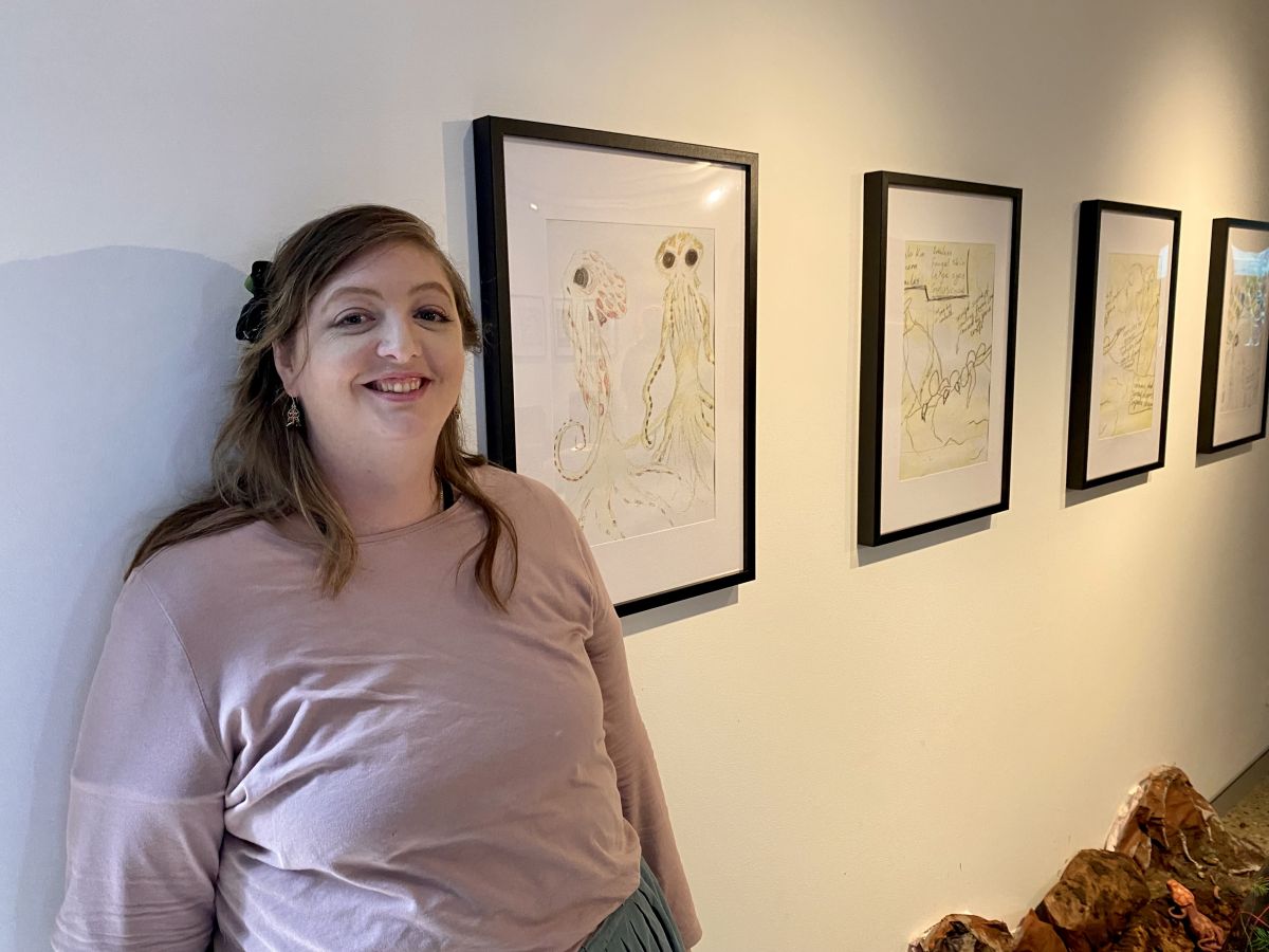 A woman stands beside a row of artworks