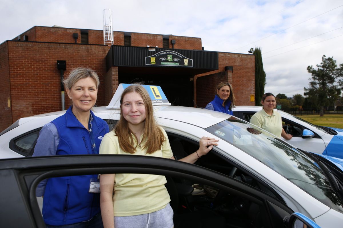 Two female driving instructors and two female high school students standing beside NRMA cars