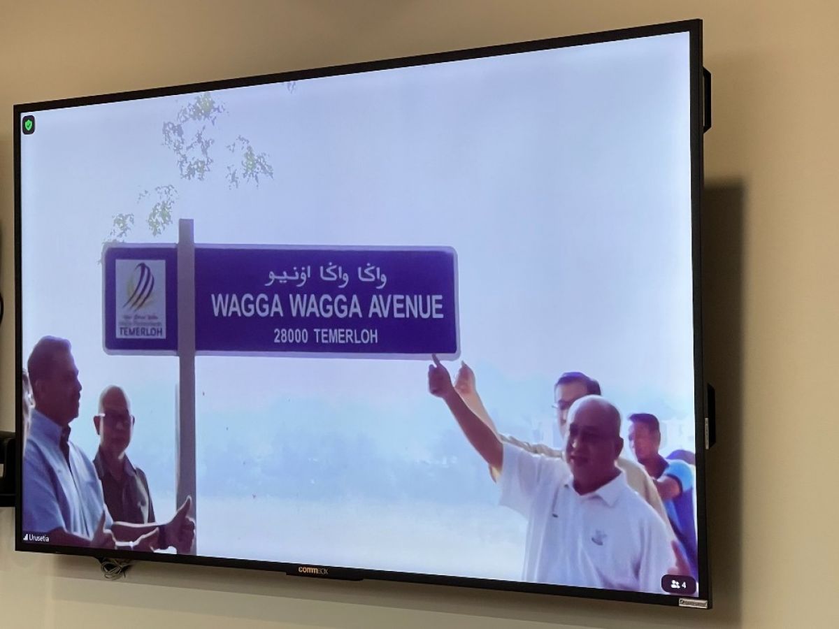 A group of men pictured on a scree, point to street sign entitled 'Wagga Wagga Avenue'