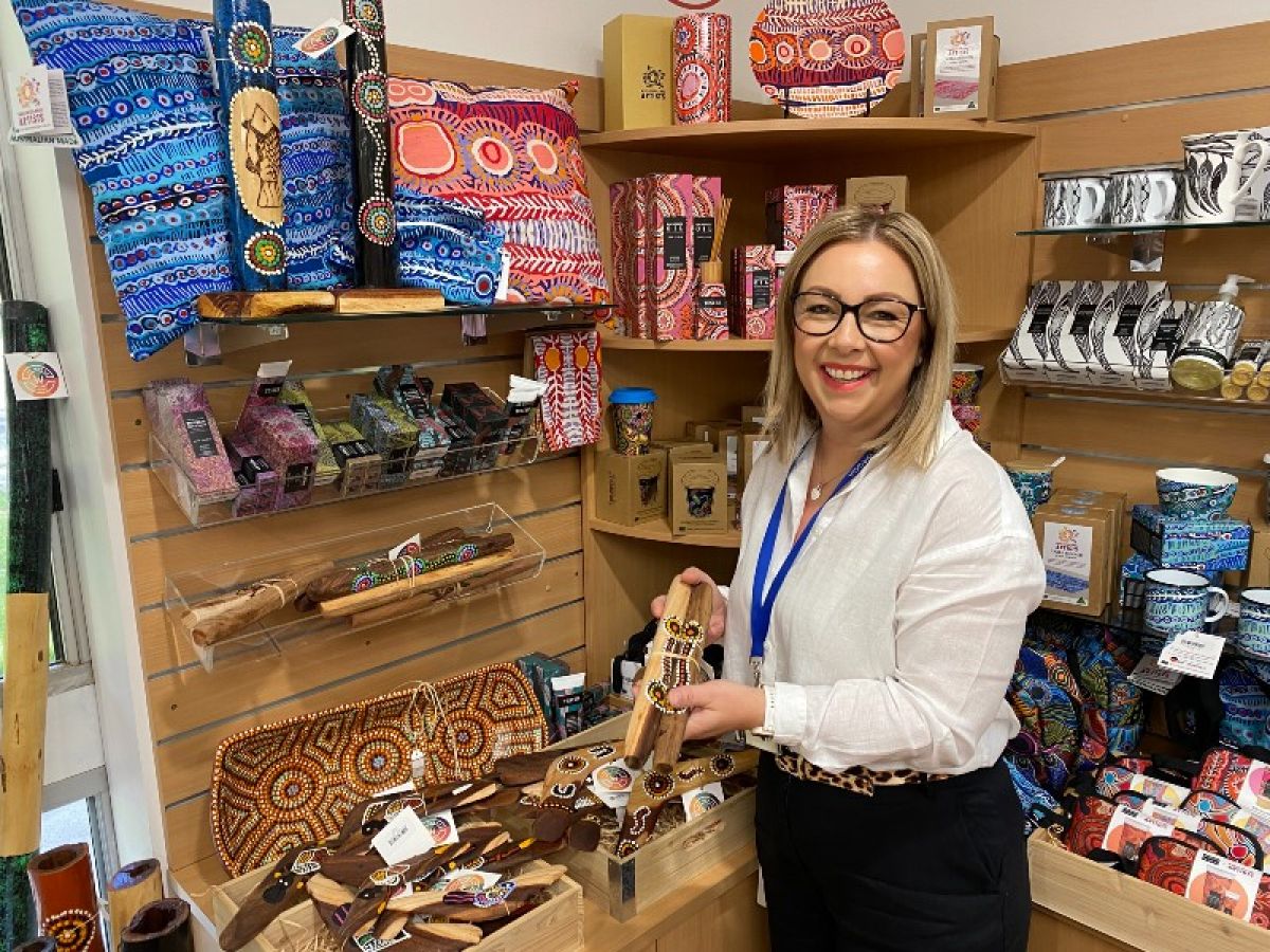 A smiling woman holding two decorated music sticks in front of a display.
