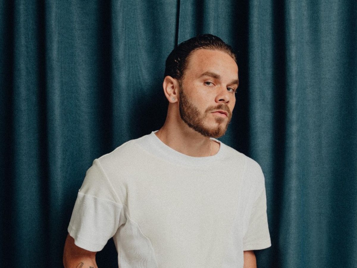 A young man stands in front of a blue curtain