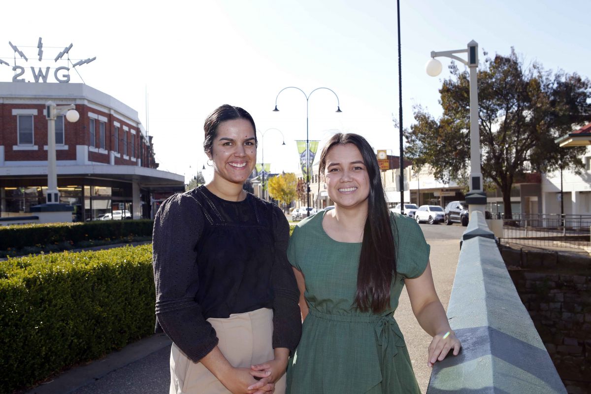 Two women standing next to bridge rail with businesses in backgrounds