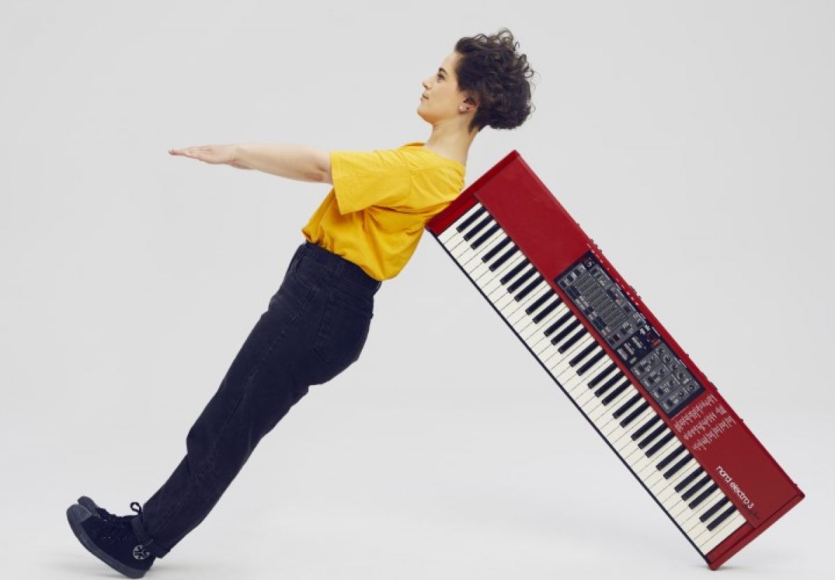 A person wearing a yellow t-shirt and black pants leaning on a keyboard, both are perpendicular to each other. 