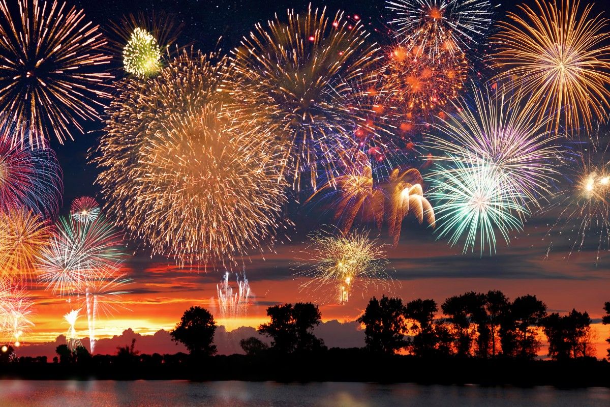 Fireworks display over water with trees in background