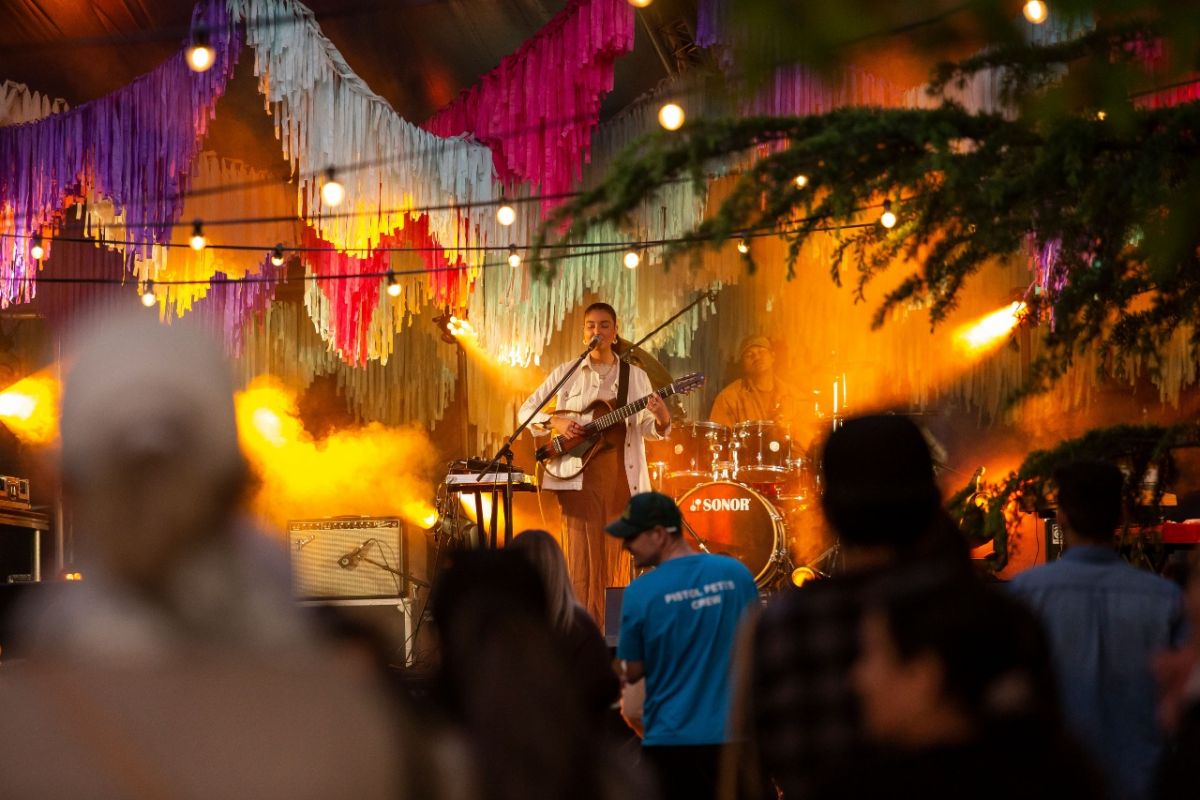 Female singer playing guitar on outdoor stage at night time