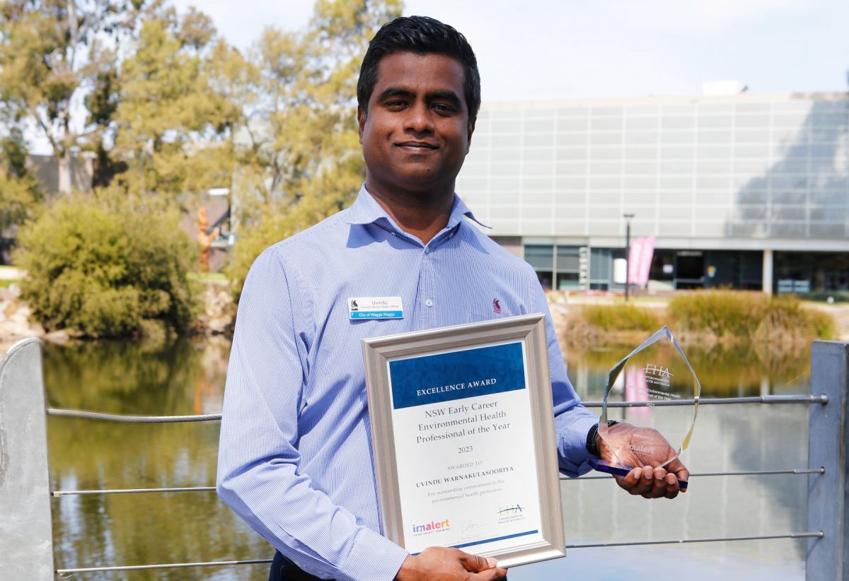 Mid shot of Uvindu holding his certificate and award in the Wollundry Lagoon precinct.