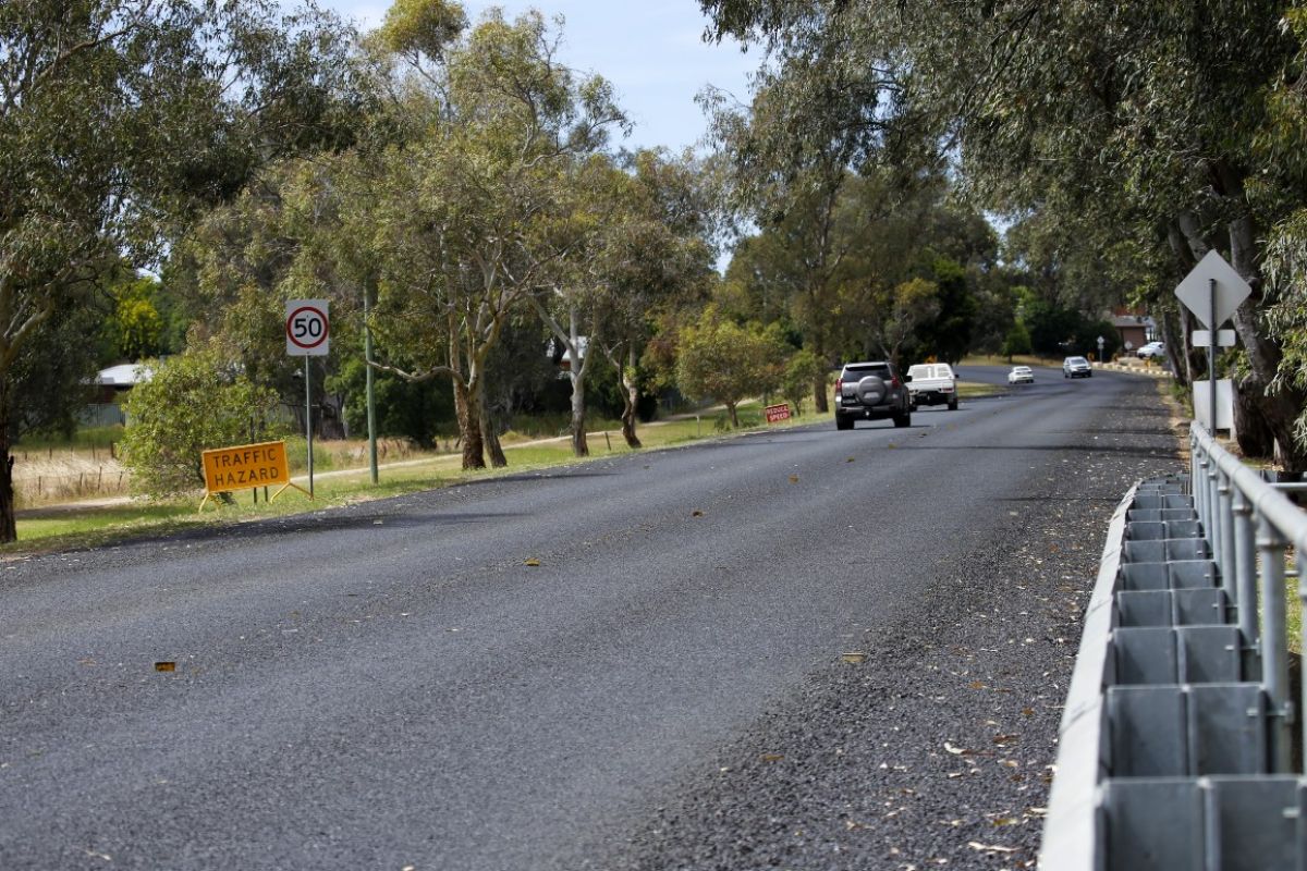 Light traffic travelling on recently sealed road, with traffic hazard sign on the left hand side of road