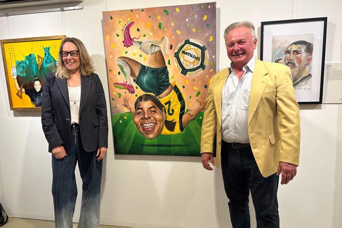 A man and a woman stand with a caricature painting of Matildas captain Sam Kerr. 